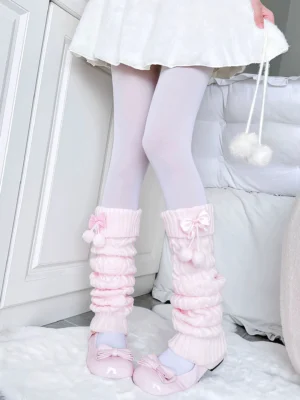 White knitted leg warmers with rose pink bow and decorative pom-poms worn with white mini dress, low angle front shot showcasing ruched fabric texture and Jirai Kei aesthetic