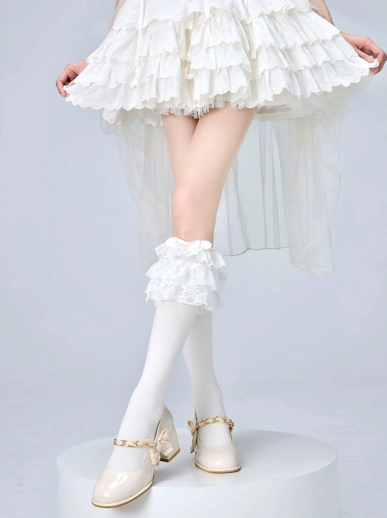 Frilled white lolita calf socks with lace ruffles and bow embellishment worn with white ruffled skirt and beige chain heels jirai kei aesthetic