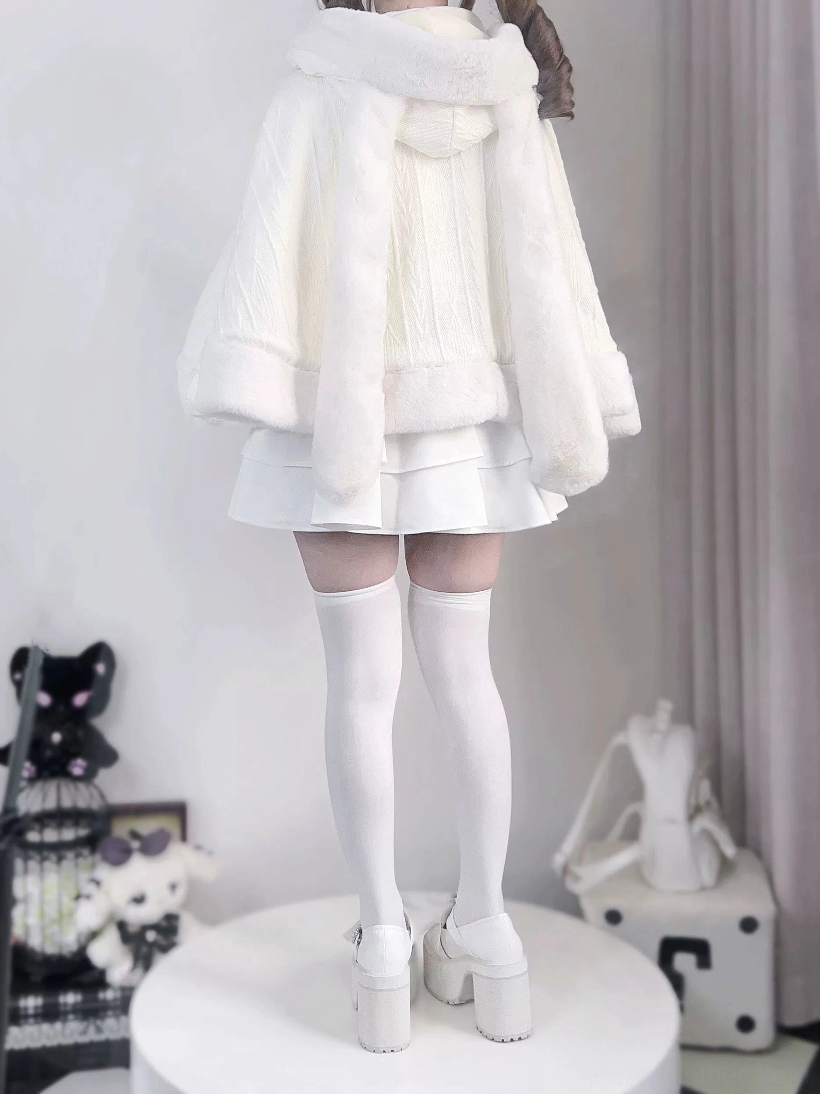 Back side angle of white rabbit ear cape with hood up covering head, curved plush hem detail, and sheer thigh-high stockings visible