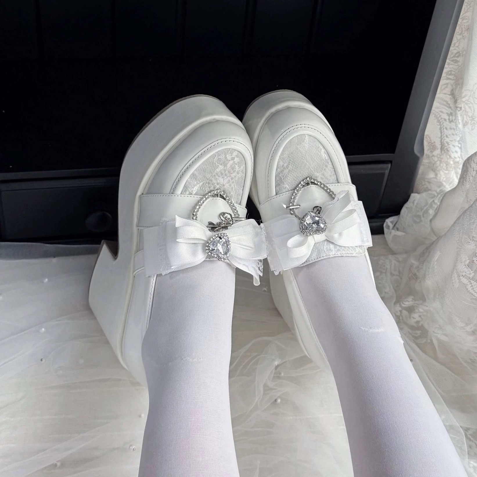 White Ryousangata platform loafers worn with white sheer tights, first-person on-foot view showing satin bow with heart rhinestone buckle