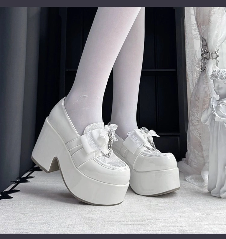 White Ryousangata platform loafers with glossy patent leather and small crystal bow ornament, low-angle side profile view on-foot with white sheer tights