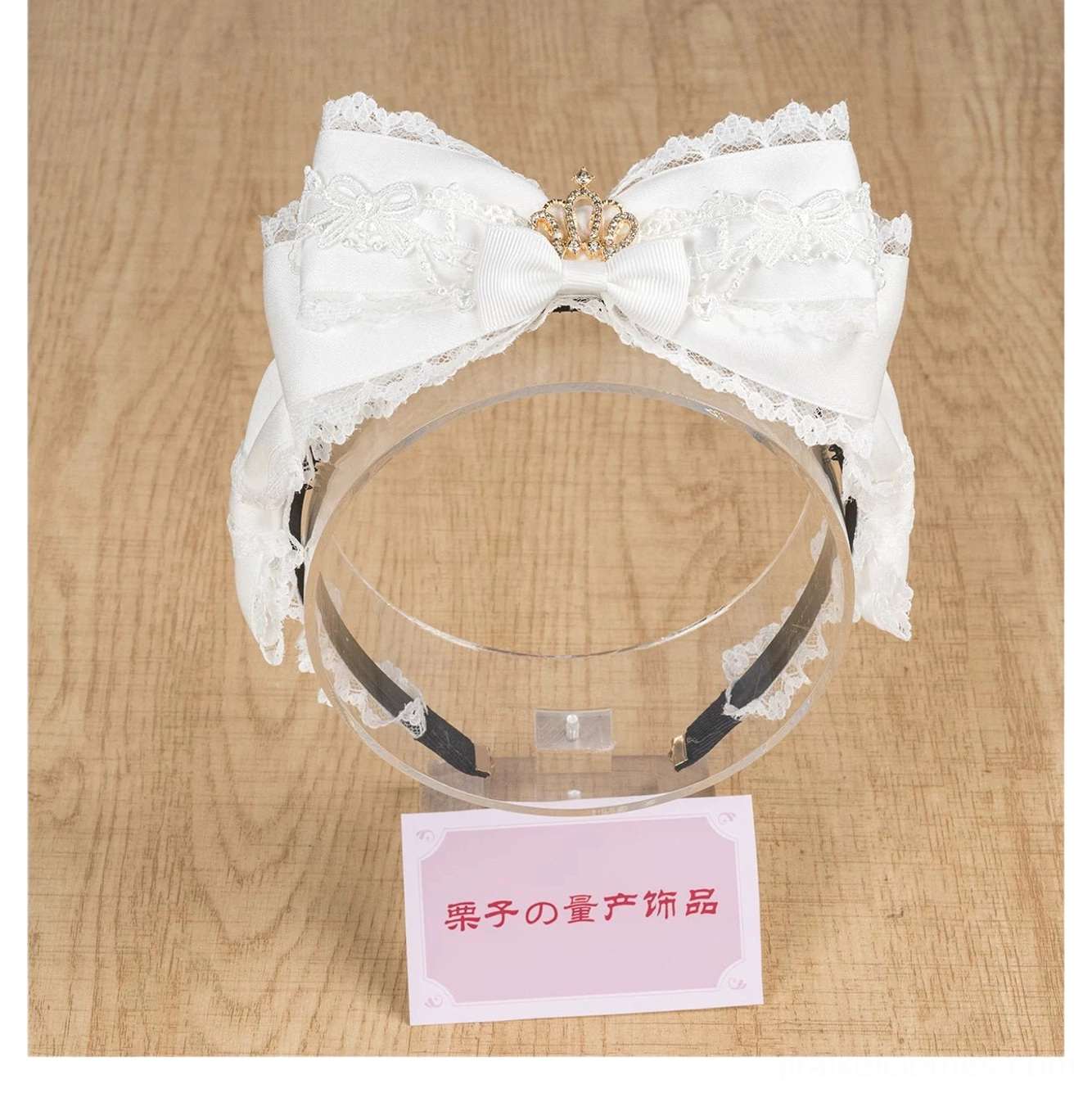 White satin lace bow headband with rhinestone crown on acrylic display stand flat front view