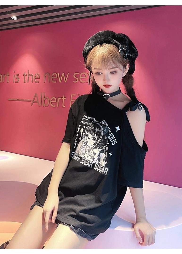 Close-up three-quarter sitting view of oversized black off-shoulder anime print graphic tee with adjustable cold-shoulder strap detail and decorative bow