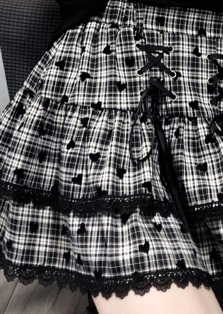 Flat lay close-up detail of black-white plaid ruffle mini skirt showing lace hem, heart-shaped decorative details, lace-up front design and plaid pattern construction