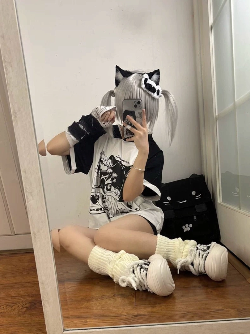 Full-length sitting mirror selfie of yami kawaii girl wearing black and white cat ear hooded anime graphic tee with loose fit, fluffy leg socks, twin light gray hair